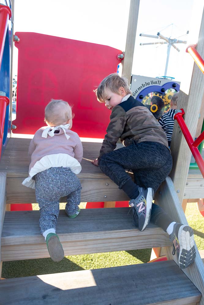 Nathan helps Emilia from Backyard Travel Family negotiate the stairs in the under 5s area of Rolleston's Foster Park Adventure Playground, Christchurch, New Zealand