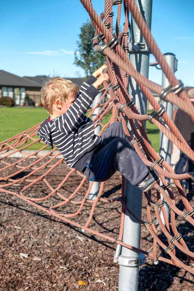 Kipton from Backyard Travel Family climbs the rope structure at Neil Graham Park Playground, next to Knights Stream School, Halswell, Canterbury, NZ