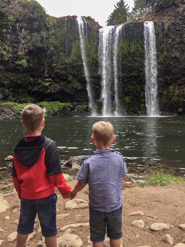 Nathan and Kipton from Backyard Travel Family hold hands as they admire Whangarei Falls, Northland