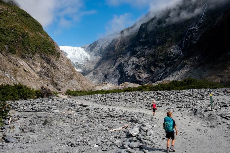 Nathan and Kipton from Backyard Travel Family walk on the Franz Josef Glacier track, as the cloud clears to reveal the icy white Franz Josef Glacier