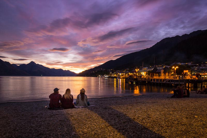 Tourists watch the sun go down on Queenstown Watefront at Sunset