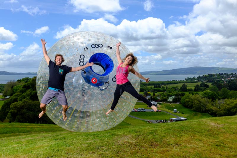 Young couple jumping in the air in excitement at the Zorb adventure activity in Rotorua