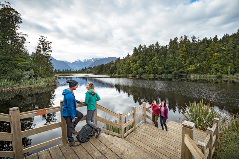 4 adults enjoying the beautiful views on the Lake Matheson walk, West Coast, NZ. Photo by Miles Holden