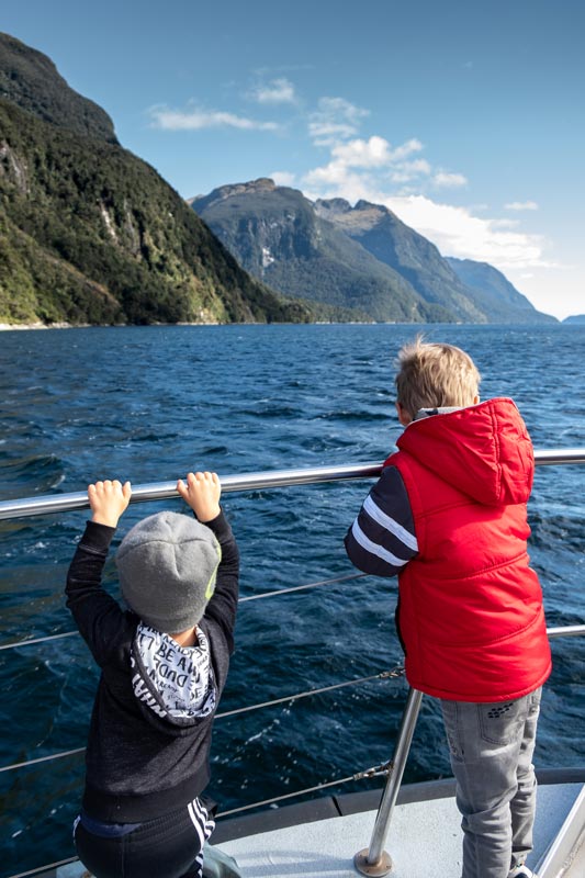 The boys lead on the boat railing, looking at the water on a beautiful day in Doubtful Sound