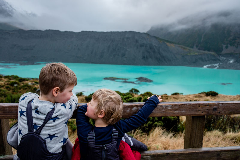 Backyard Travel Family kids smile at each other as they look at the turquoise Mueller Lake in Mt Cook National Park