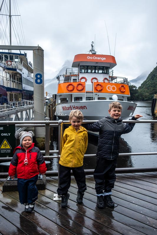 Backyard Travel Family kids stand in front of the Milford Haven at the dock, prior to their Milford Sound Cruise