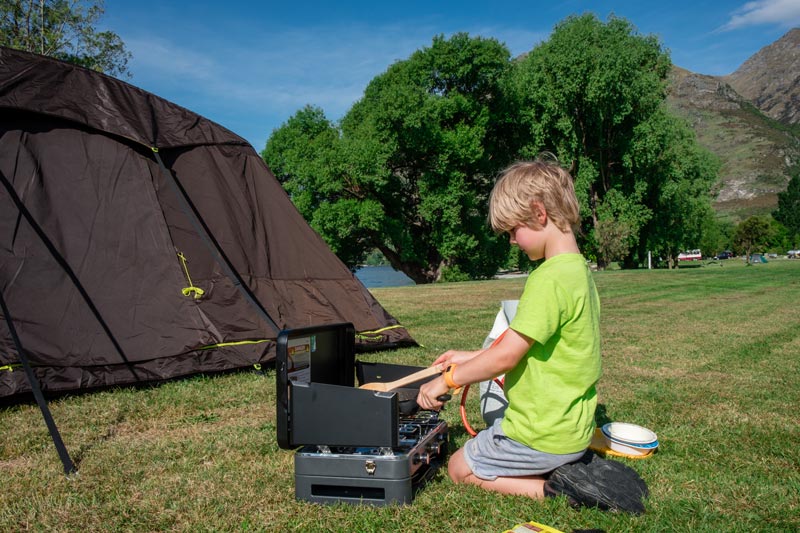 Nathan from Backyard Travel Family cooks a camping dinner on his Zempire Deluxe Cooker with grill