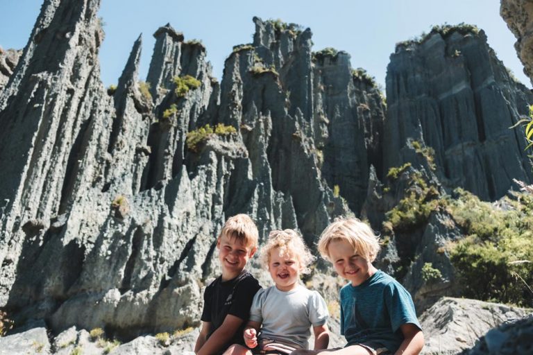 3 happy kids sitting in front of the Putangirua Pinnacles, unique rock formation in the Wairarapa