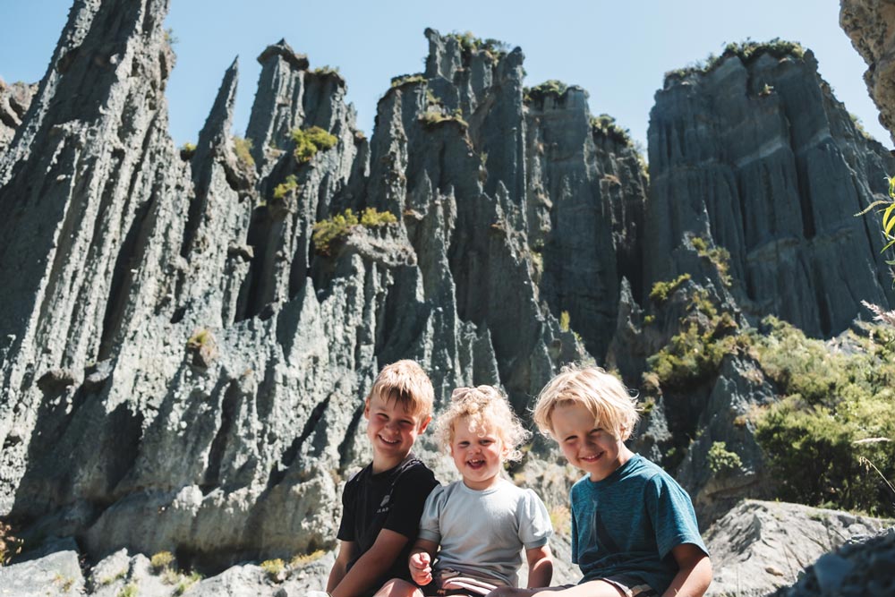 3 happy kids sitting in front of the Putangirua Pinnacles, unique rock formation in the Wairarapa