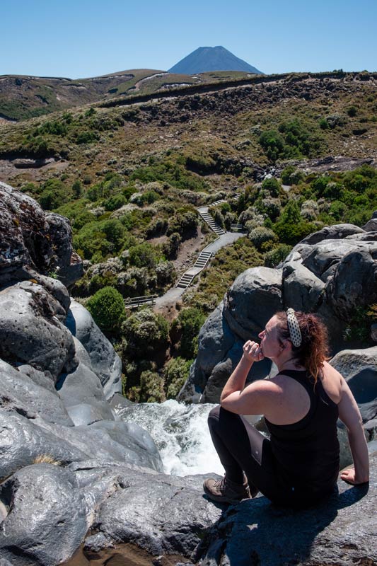 Jen from Backyard Travel Family sits at the top of Taranaki Falls overlooking the Taranaki Falls track in Tongariro National Park