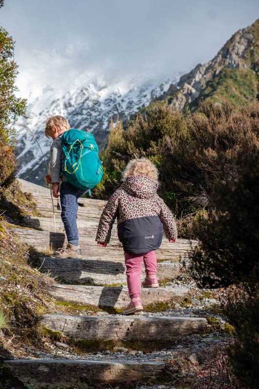 2 children walk up the stairs on the Red Tarns Track, with a snowy mountain backdrop
