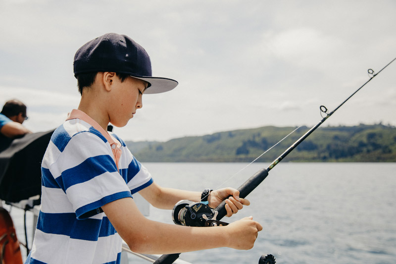 A boy looks down at his fishing road, while boating on Lake Taupo, New Zealand