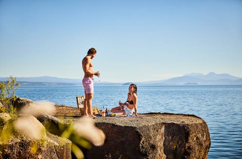 A couple drink wine and have a picnic by Lake Taupo New Zealand