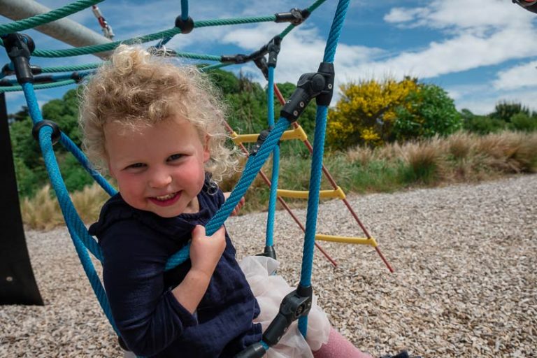 Emilia sits on a rope swing at South New Brighton Playground, one of the best playgrounds in Christchurch