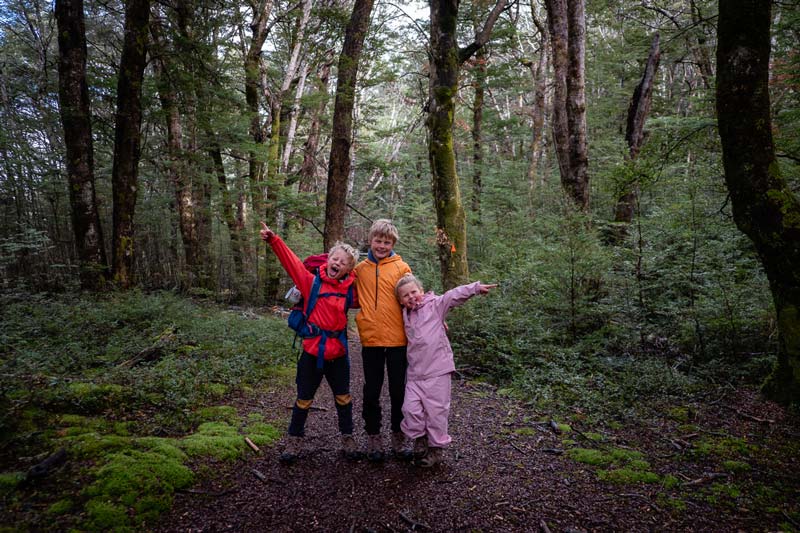 3 kids give big smiles in the native bush on their way to Kiwi Burn Hut in Fiordland