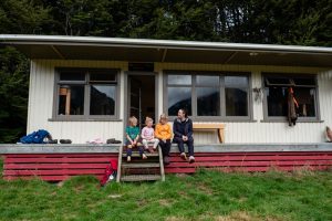 Wide angle of Kiwi Burn Hut with Backyard Travel Family sitting on the deck in front