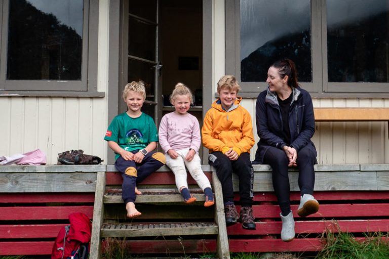 Backyard Travel Family sit on the decking outside Kiwi Burn Hut and smile for the camera