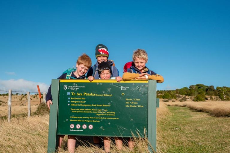Kids lean on the DOC start sign at the beginning of the Rod Donald Hut track