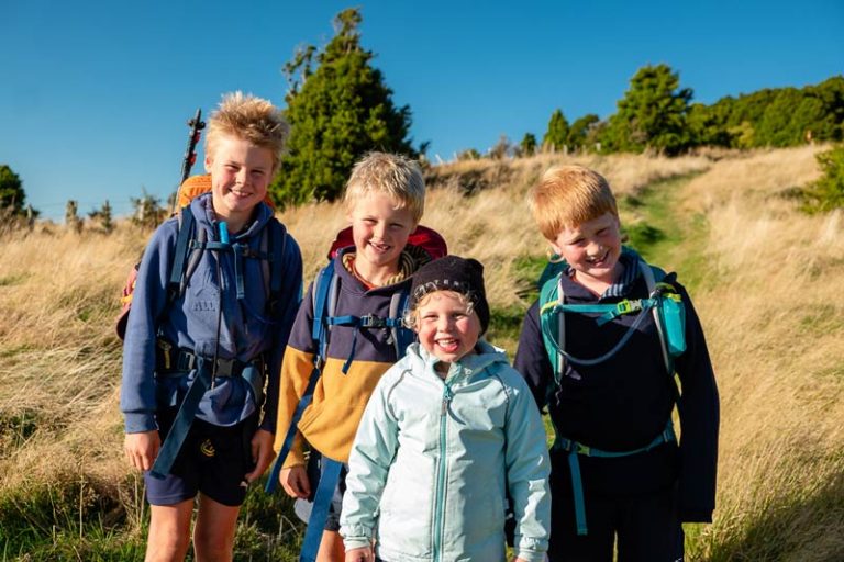 4 kids with backpacks on smile as they are ready to walk the Rod Donald Hut Christchurch